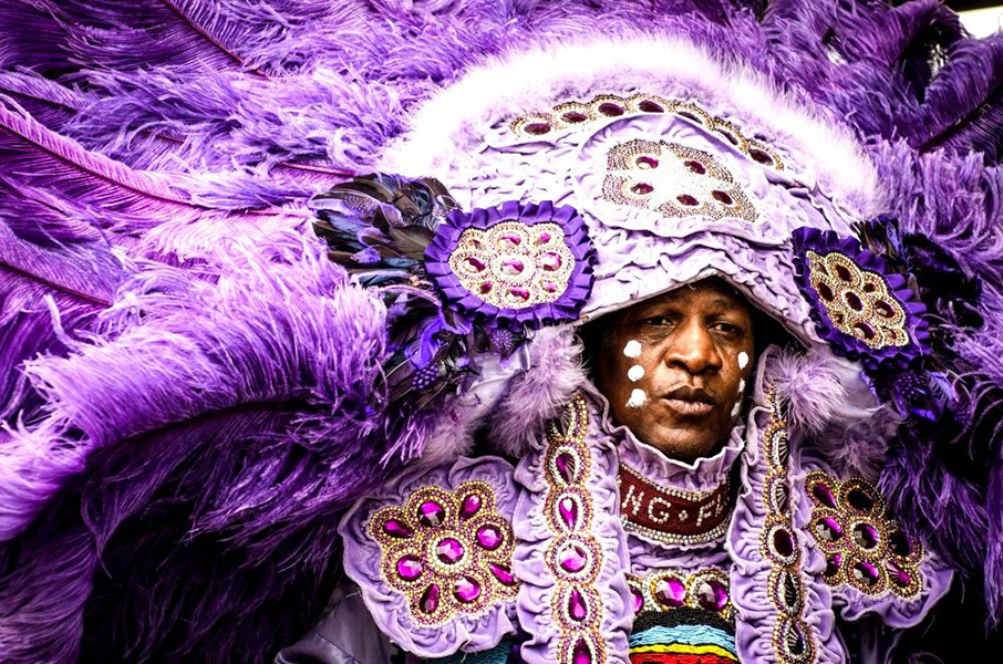 Mardi Gras Indian dressed in a purple suit adorned with feathers, jewels, and beads.