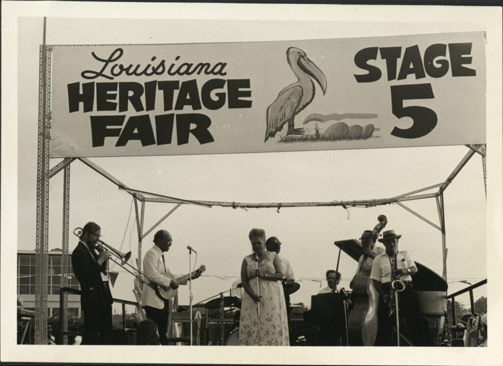 Louisiana Heritage Fair Stage 5, with band featuring Danny Barker, banjo; Blue Lu Barker, vocals; and Frank Naundorf, trombone, 1974, Jazz Fest, photographer unidentified, Mina Lea Crais collection HJA-060, 117.090, Tulane University Special Collections.