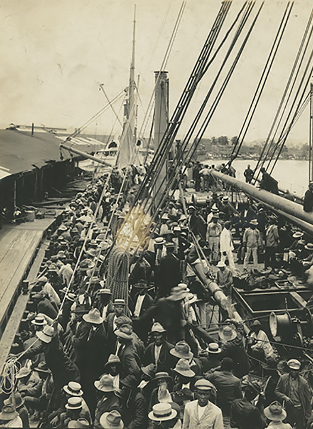A docked ship with people crowded on the deck.
