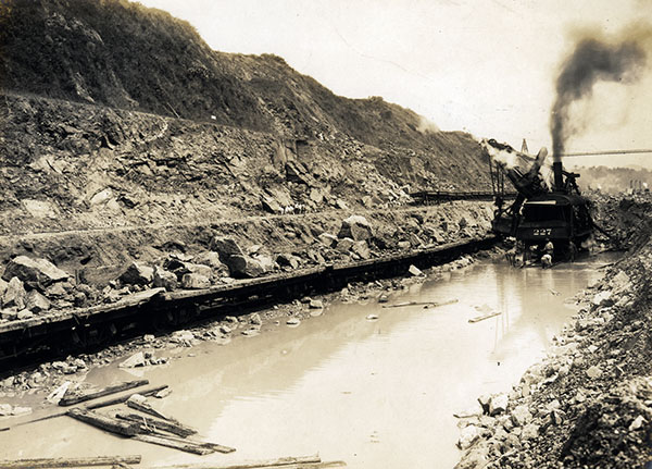 Machinery surrounded by shallow water in an excavated mountain range.