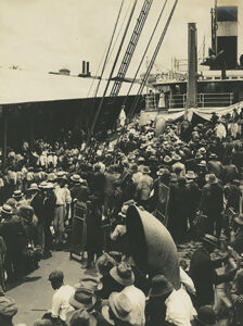 A docked ship with people crowded on the deck.